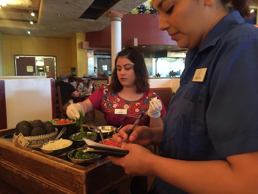 Tortilla Jo employees preparing fresh guacamole with avocados, onions, tomatoes and other ingredients on a table. 